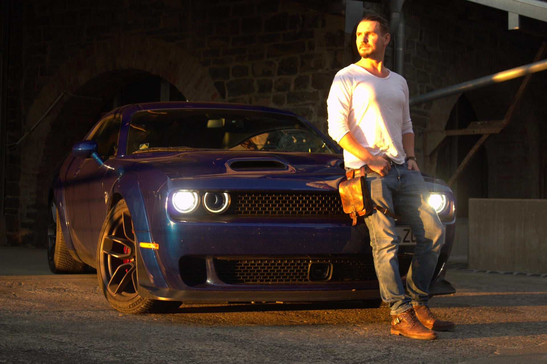 Rudolf leaning on his blue Dodge Challenger Hellcat at sunset